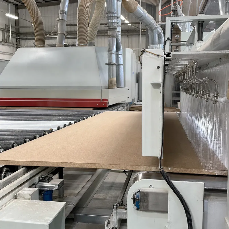 In-line primer application station on hardboard production line — panel moves directly from wide-belt sander to primer coating without leaving the controlled environment