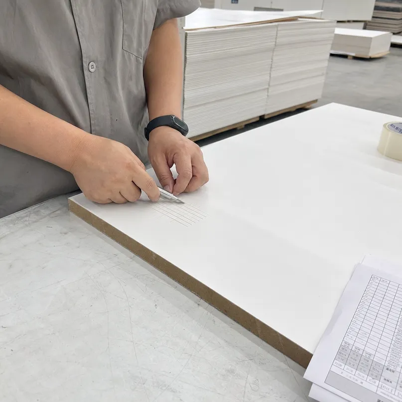Quality control cross-cut adhesion test on primed hardboard panel at QDPlywood factory