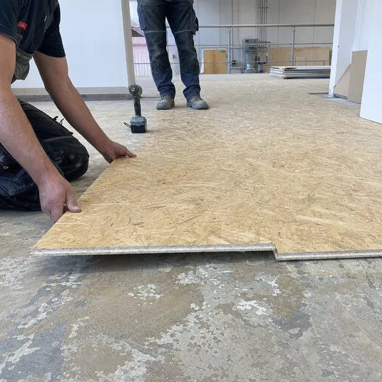 OSB flooring panel being installed as overlay over existing floor during renovation
